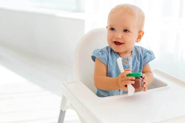 Bebê fofo e engraçado com uma colher nas mãos comendo purê de frutas