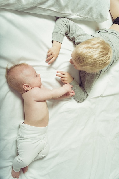 Bebê fofo e irmão mais velho interagem enquanto estava deitado na cama. Vista do topo