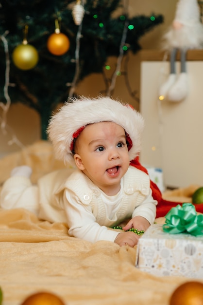 Bebê fofo e sorridente está deitado sob uma árvore de natal festiva e brincando com presentes. celebrações de natal e ano novo.