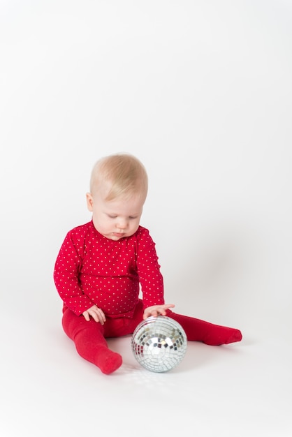Bebê fofo em roupa vermelha brincando com uma bola de festa