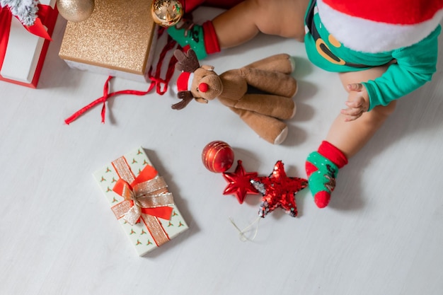 Bebê fofo em uma roupa verde e um chapéu de Papai Noel decora a árvore de Natal com balões coloridos. criança em uma fantasia de gnomo de Natal. conceito de ano novo de inverno. espaço para texto. vista do topo