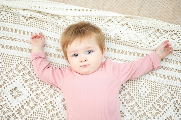 Bebê fofo está deitado na cama de costas com roupa de cama branca no quarto da casa retrato de uma criança que a criança está olhando para a câmera