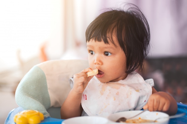 Bebê fofo menina criança asiática comendo comida saudável sozinha