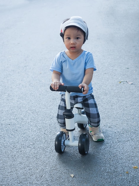 Bebê fofo menino asiático com capacete de segurança e protetor de cabeça aprendendo a andar com sua primeira bicicleta de corrida branca na estrada