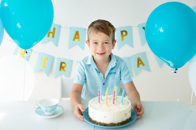 Bebê fofo menino comemora aniversário com balões azuis e um bolo de aniversário doce em um fundo branco Feliz aniversário