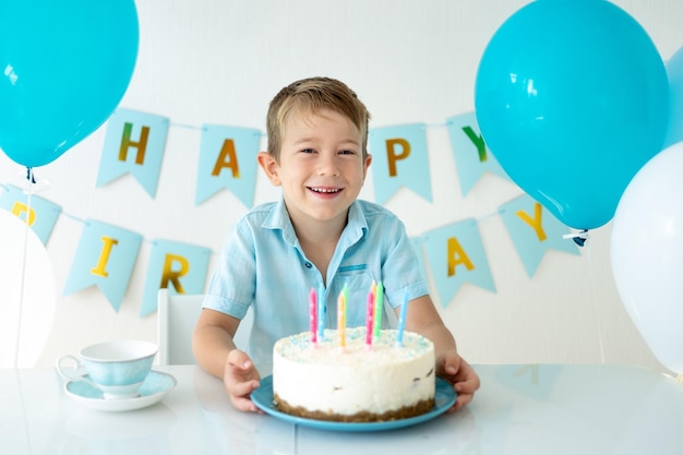 Bebê fofo menino comemora aniversário com balões azuis e um bolo de aniversário doce em um fundo branco feliz aniversário