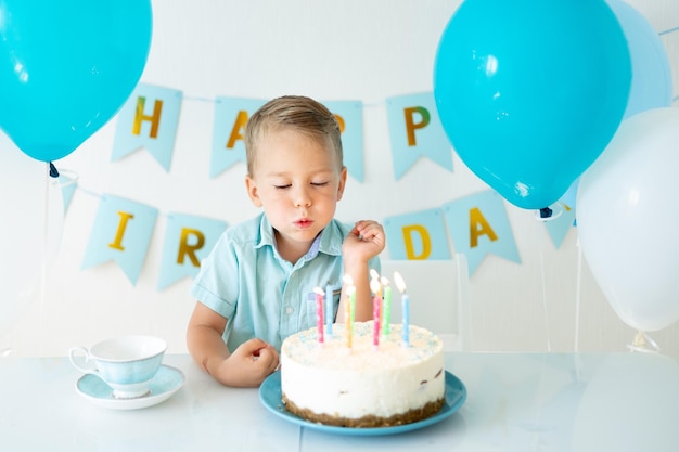 Bebê fofo menino comemora aniversário com balões azuis e um bolo de aniversário doce em um fundo branco Feliz aniversário