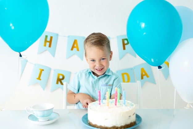 Bebê fofo menino comemora aniversário com balões azuis e um bolo de aniversário doce em um fundo branco feliz aniversário