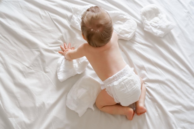 Bebê fofo na fralda macia seca na cama branca em casa vista superior Foto de alta qualidade