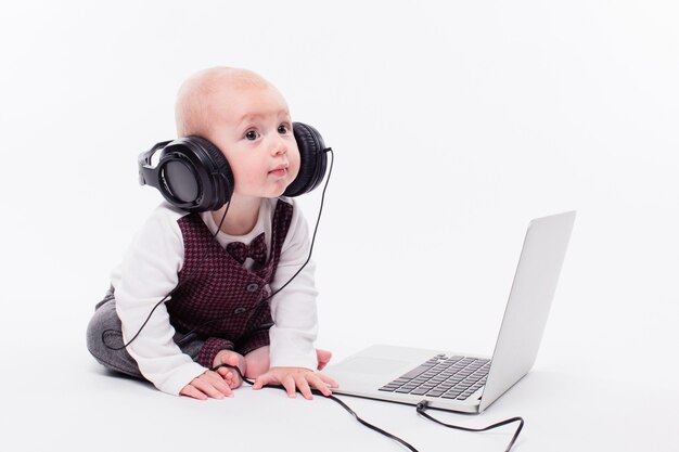 Bebê fofo sentado na frente de um laptop usando fones de ouvido