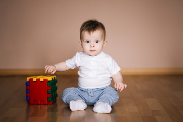 Bebê fofo sentado no chão da casa brincando com um cubo multicolorido