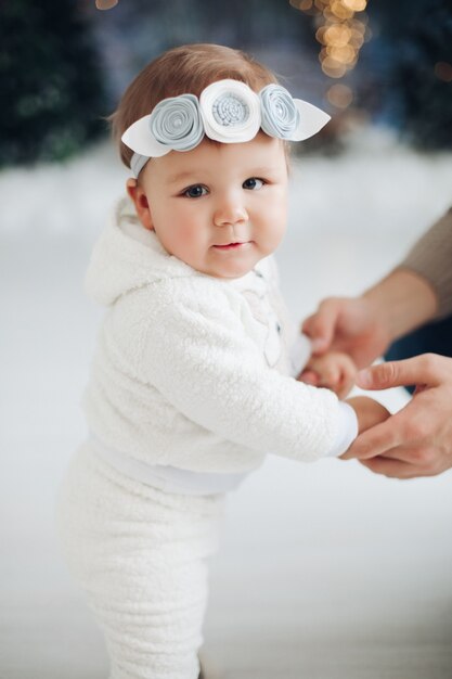 Bebê fofo vestido de branco em pé com apoio de adulto