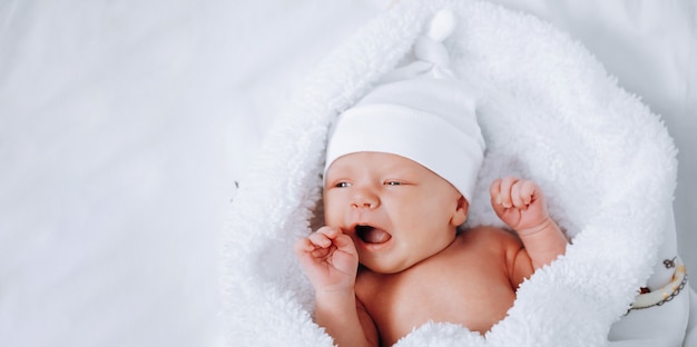 Bebé con una gorra blanca sobre una manta blanca. bostezos recién nacidos