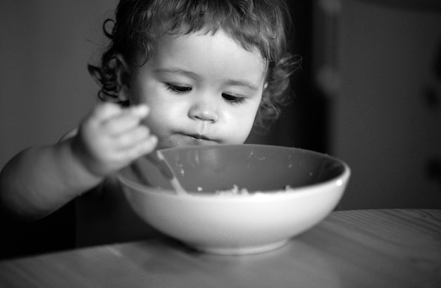 Un bebé gracioso en la cocina comiendo con los dedos del plato.