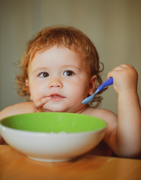 Foto bebé gracioso comiendo comida él mismo con una cuchara en la cocina nutrición saludable para niños