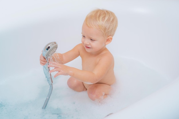 Bebé gracioso jugando con agua y espuma en un gran fregadero de cocina niño hermoso con baño de burbujas