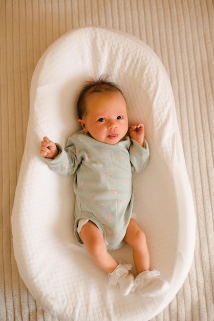 Bebê infantil bonitinho com menos de 1 ano deitado na cama berço vestindo pijama na sala de casa no quarto Pequena menina recém-nascida acorda olhando para a câmera Infância