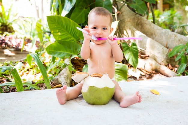 Bebê infantil feliz em férias tropicais Come e bebe coco verde jovem Senta-se no chão