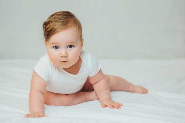 Foto bebé infantil lindo en el bebé blanco que aprende sentarse.