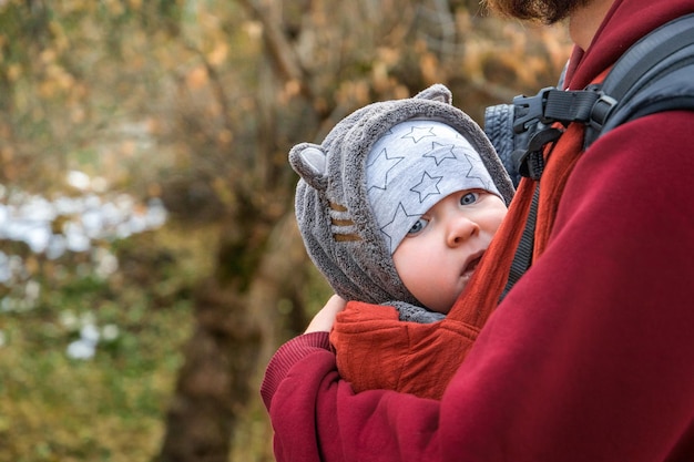 Bebê jovem viajante em estilingue ergonômico na natureza do outono