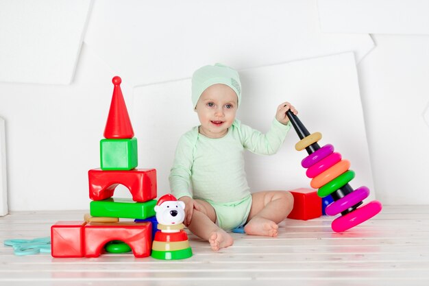 El bebé juega con juguetes en la habitación de los niños en casa con un mono verde, el concepto de desarrollo y ocio de los niños pequeños