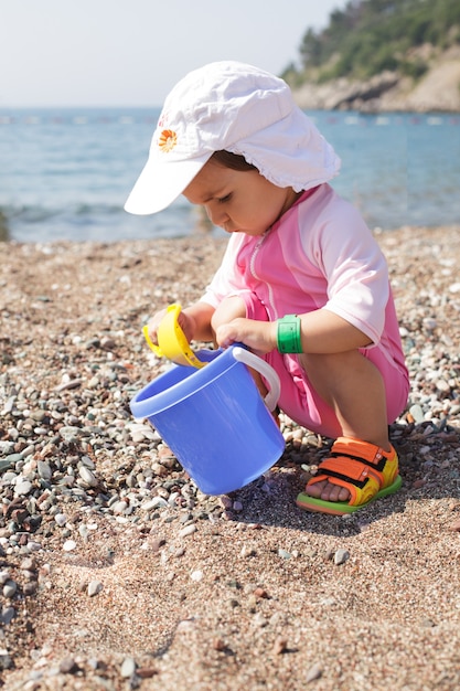 Bebé juega en la orilla del mar con rebbles y balde