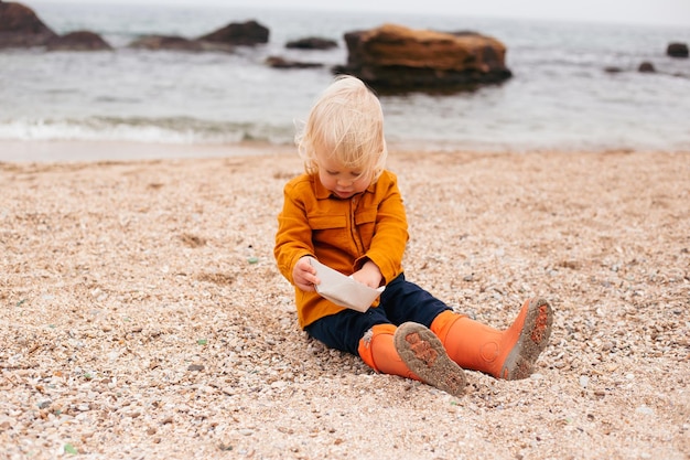 El bebé jugando con un bote de papel en la playa en otoño