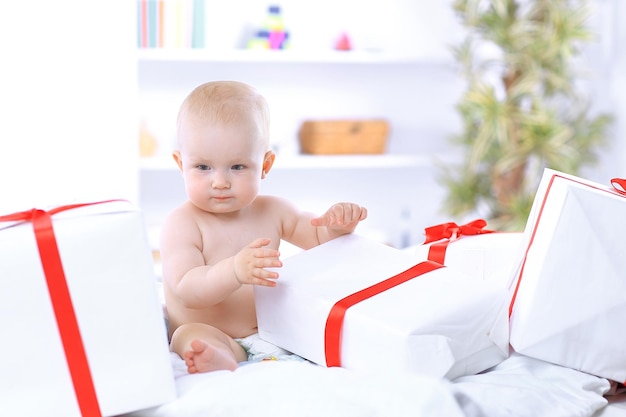 bebê lindo brincando com caixas de presente sentado no sofá