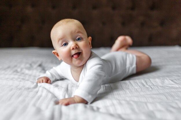 Bebé lindo divertido en un traje de luz blanca en la cama en casa mirando