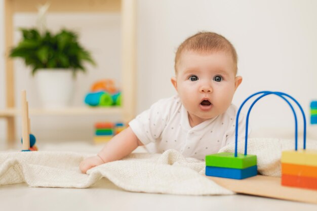 Un bebé lindo está acostado boca abajo sobre una manta de lino gris y jugando con juguetes educativos de colores. productos para niños. concepto de una infancia feliz y maternidad. cuidado de los niños. espacio para texto