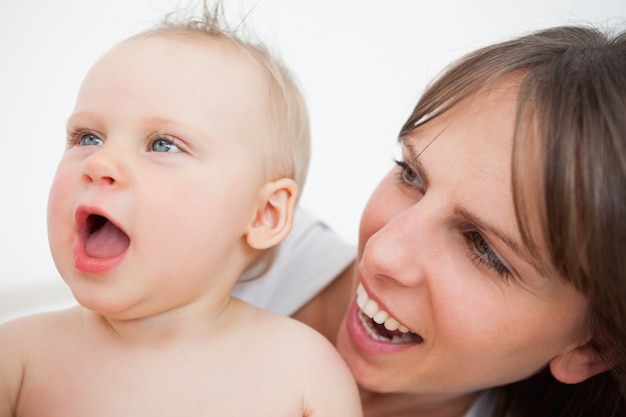 Bebé lindo que abre su boca mientras que es sostenido por su madre