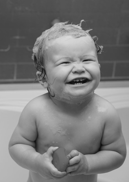 Bebê lindo sorridente tomando banho no chuveiro bebê engraçado banhado em espuma e lavando na banheira em casa