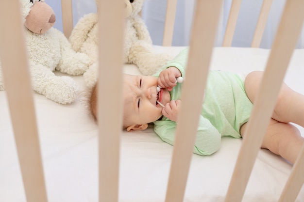 Un bebé llorando en una cuna con un mordedor en el dormitorio.