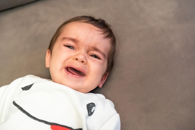 Foto bebé llorando con el dolor de sus primeros dientes, acostado en el sofá de casa