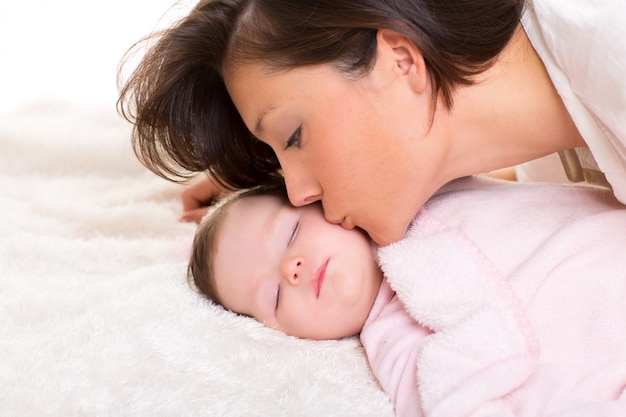 Foto bebé y madre que la besan mentira feliz en blanco