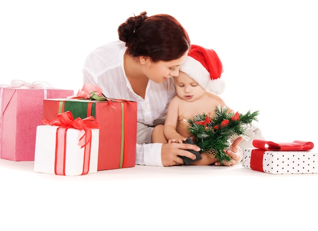 El bebé y la madre con regalos de Navidad sobre pared blanca.