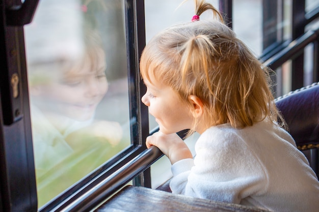 el bebé mira por la ventana y sonríe. Hermosa chica en la ventana grande. Bebé se encuentra con su hermana.