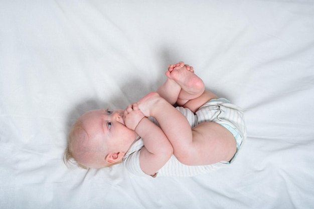 Bebê mordisca a perna na cama branca Lindo bebê de 3 meses