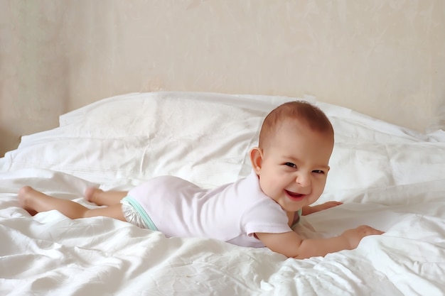 Un bebé muy feliz está acostado en una cama blanca sobre su estómago