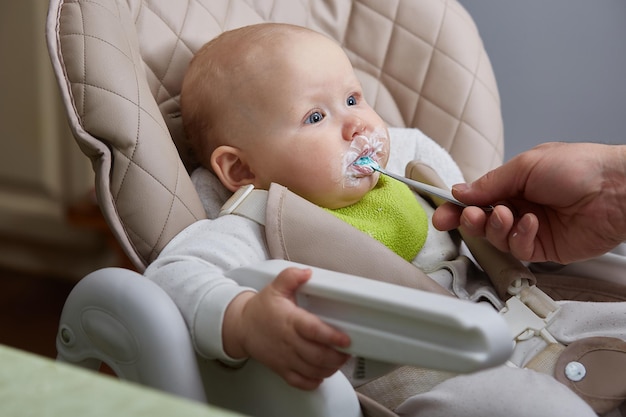 bebê na cadeira de criança come pela primeira vez de uma colher.