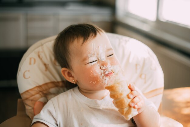 Bebê na cozinha comendo ansiosamente os deliciosos chifres de creme, recheados com um creme de baunilha muito engraçado