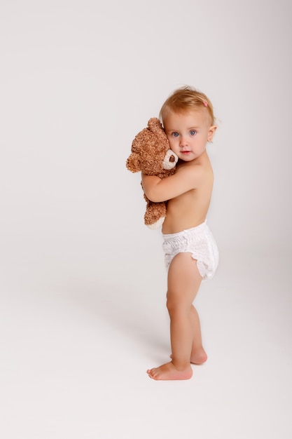 Bebé na fralda que joga com o urso de peluche no branco.