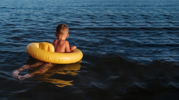 El bebé nada con un círculo amarillo inflable en el mar En la foto, el bebé está de espaldas mirando al horizonte Lugar para el texto