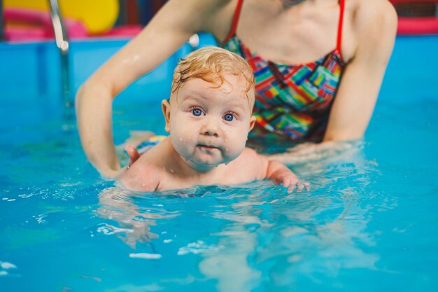 Bebé nadando en la piscina Enseñando a un niño recién nacido a nadar en una piscina con un entrenador