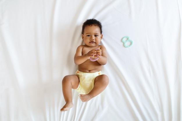 Foto bebé negro usando pañales reutilizables jugando con juguetes mientras está acostado en la cama