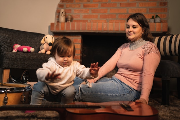 Bebé niña tocando la guitarra con su madre.