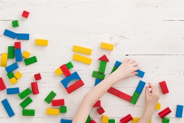 Bebé niño o niña juega con ladrillos de colores en una mesa de madera blanca Vista superior de ladrillos de madera