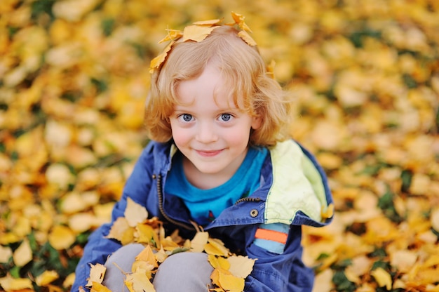 Foto bebé - niño pequeño con el pelo rubio rizado sonriendo contra las hojas amarillas de otoño en el parque