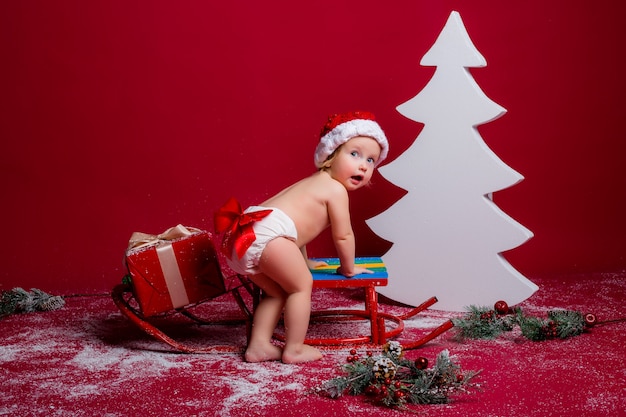 Bebê no chapéu de Papai Noel na parede vermelha