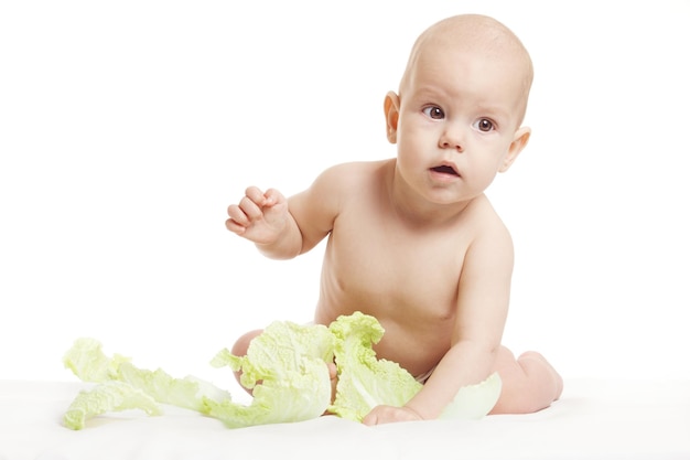 Bebê nu na fralda está brincando com frutas e legumes orgânicos frescos isolados em um fundo branco Criança mordendo uma cabeça verde fresca de repolho Comida saudável para o conceito de crianças
